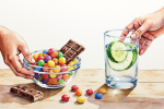 Zuckerkonsum reduzieren & Zucker-Schäden stoppen Schale mit Süßigkeiten und Glas Wasser